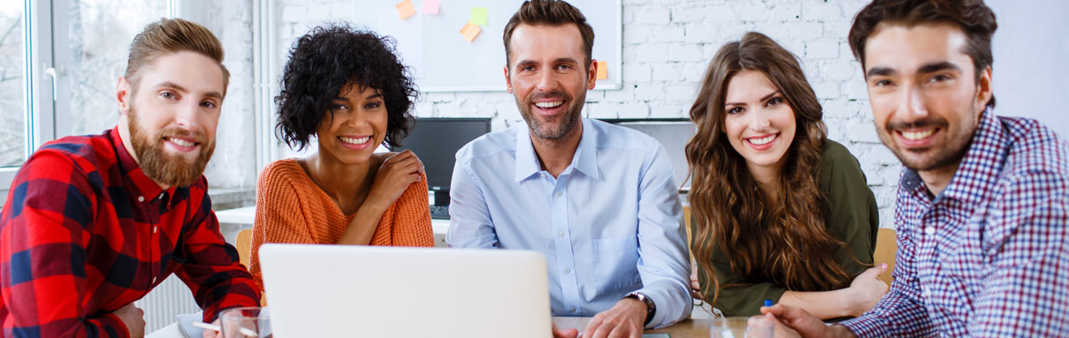 A group of adult learners with a laptop in front of them, smiling at the camera.