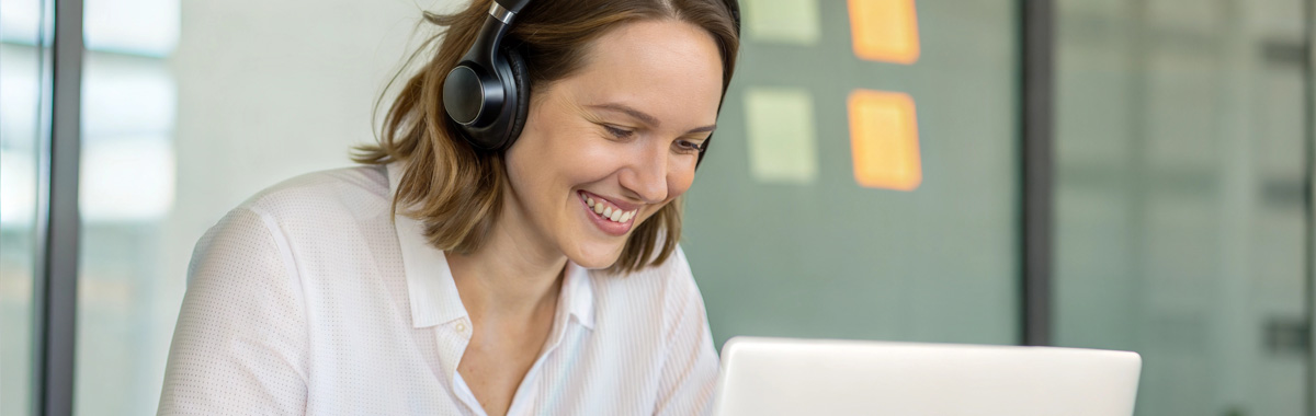 A woman wearing headphones and smiling while using a laptop.
