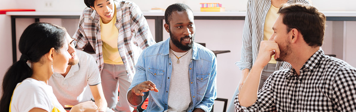 A group of teachers talking, one with a laptop and another holding a notepad.