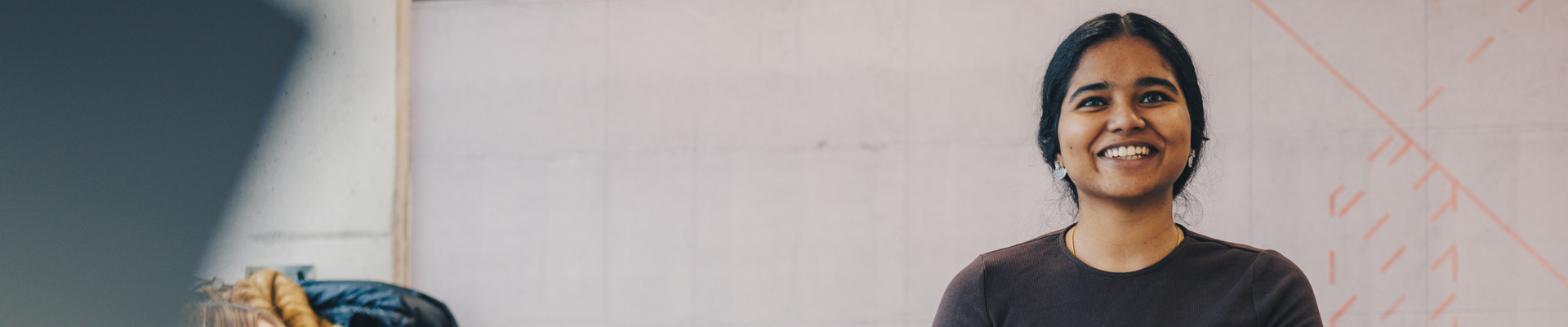 A student standing behind a table with laptops open on it, and a flipchart behind her.