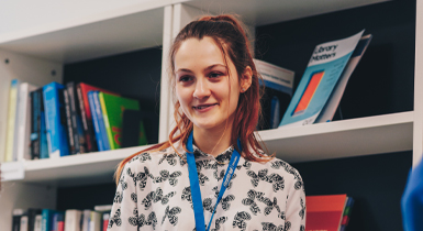A student smiling in front of a row of bookshelves.