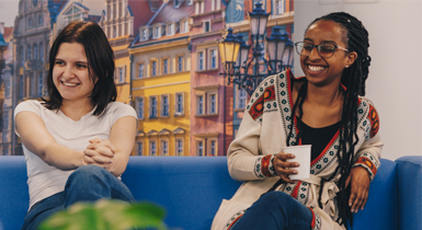 Two students sat on a blue sofa with a large photograph of the city of Wrocław in the background.