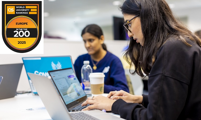 two students sitting at a desk using a laptop